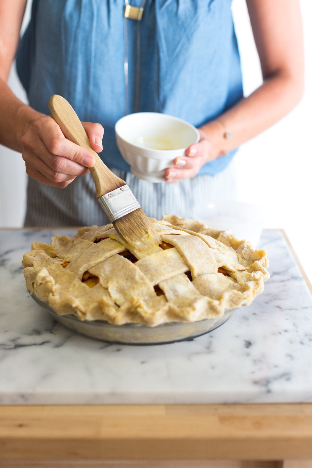 A baker brushing a peach pie with an egg wash.