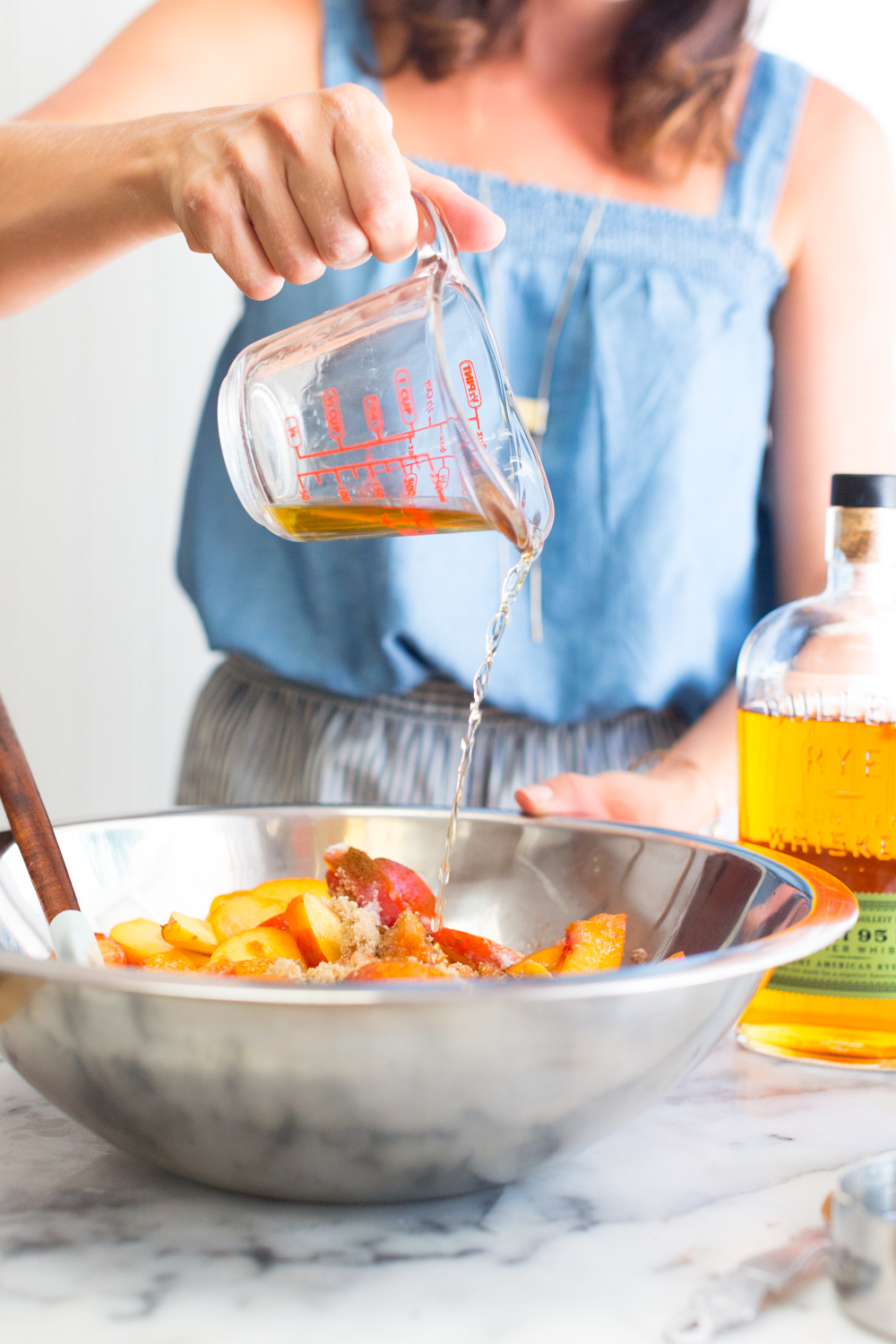 A baker pours rye whiskey into a mixing bowl of peach pie filling