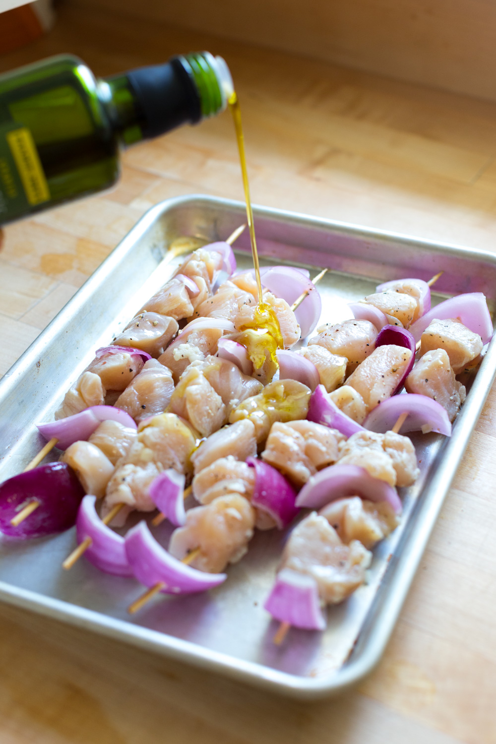 Drizzle the feta brined chicken skewers with olive oil.