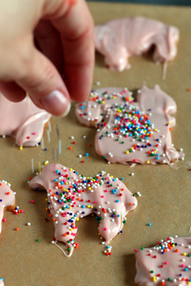 adding rainbow sprinkles to a pink animal cookie