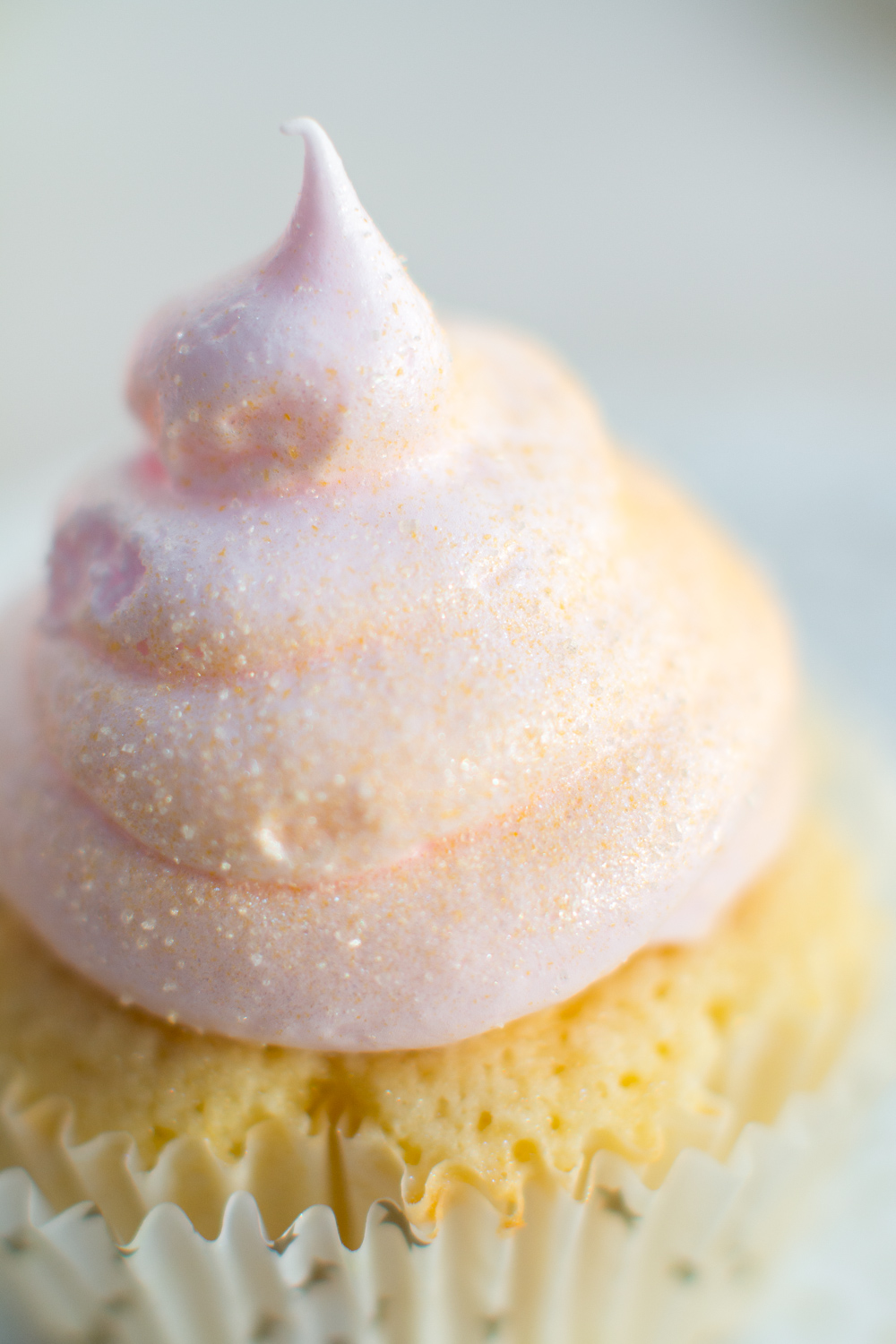 an extreme close up of edible gold dust adorning the meringue swirl atop a pink champagne cupcake