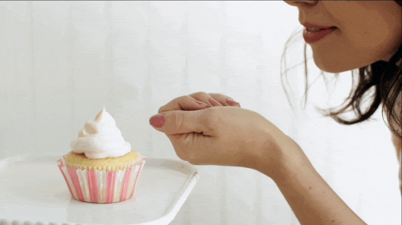 Becky Sue blows edible gold dust from her palm onto the meringue of a cupcake