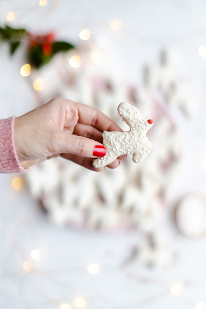 Reindeer Animal Cookie in hand, close up with cookies and holiday lights in the background