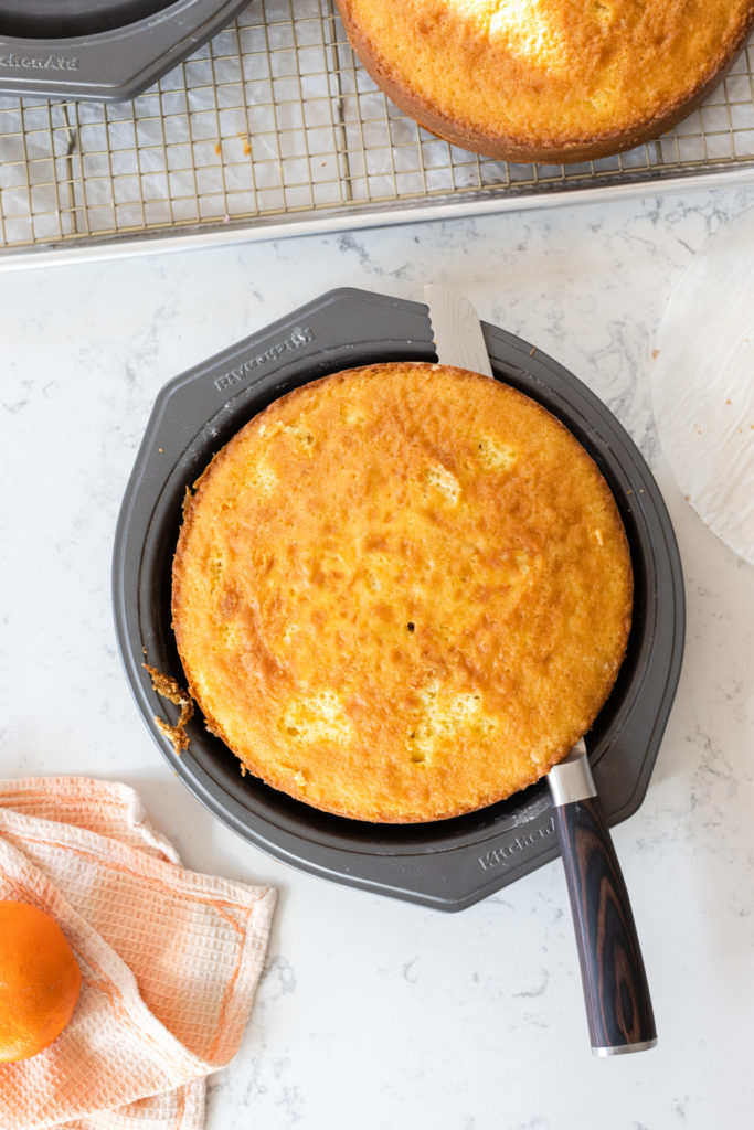 leveling a cake layer using a bread knife to remove the dome
