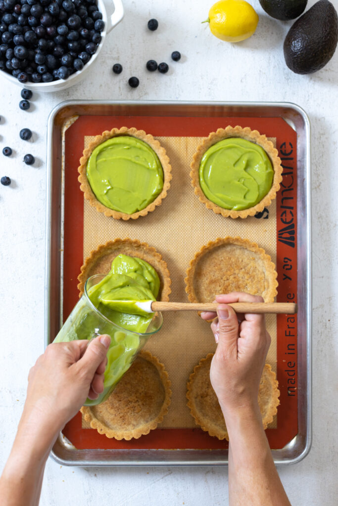 Pouring avocado filling into almond tart shells
