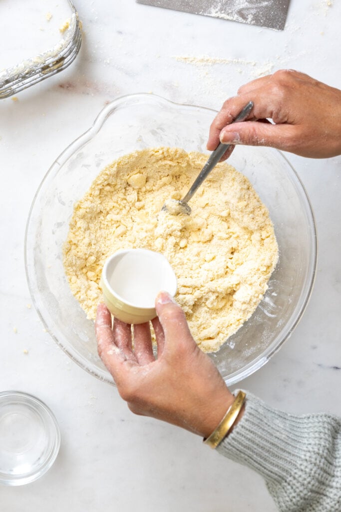 Adding vodka to Pie Dough - pouring from a small container into the mixing bowl and using a fork to mix in the vodka