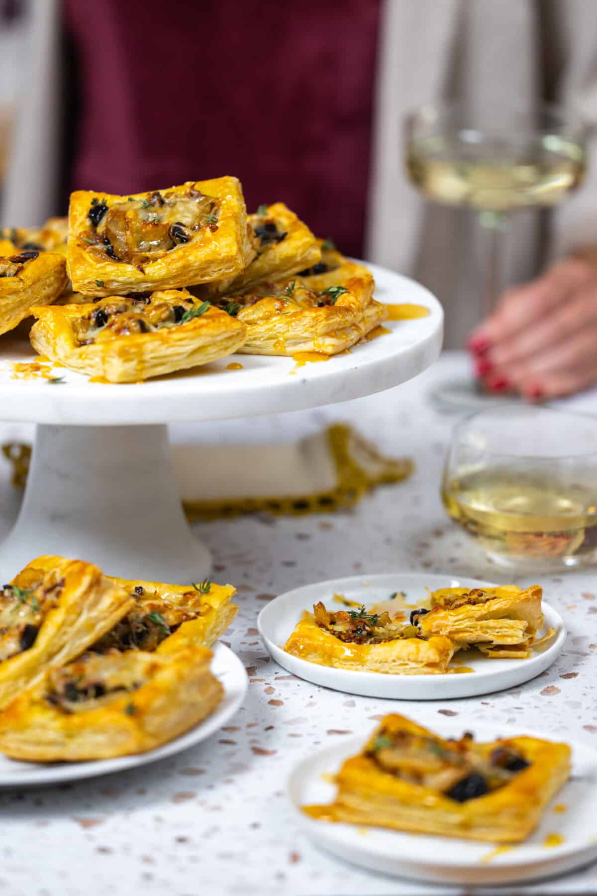 Prune Onion Fontina Tarts piled on a marble cake stand - styled angled shot with party drinks