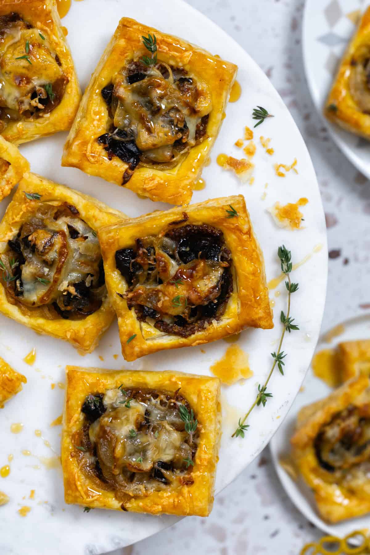 Prune Onion Fontina Puff Pastry Tarts close up arranged on a decorative marble cake stand
