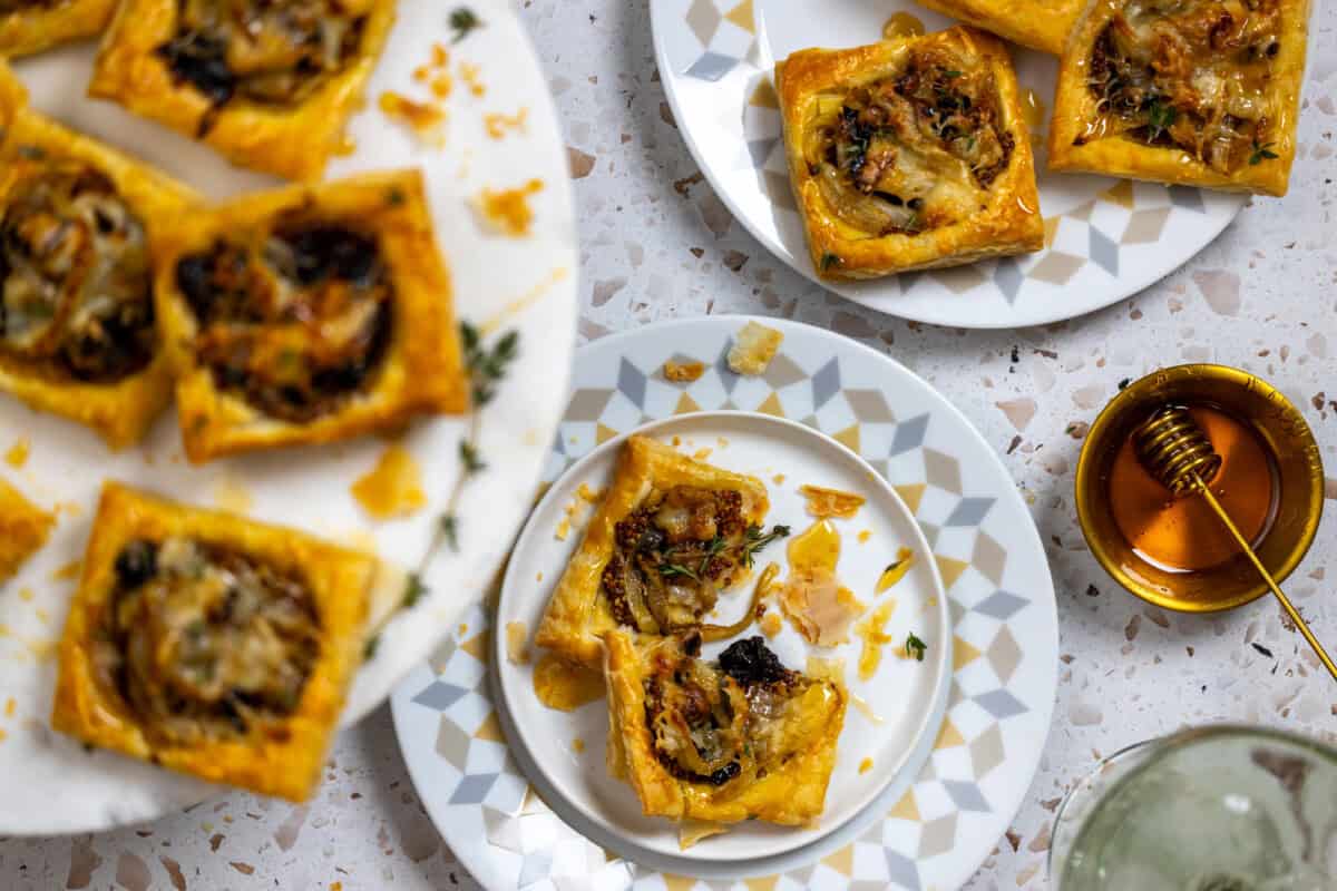 Flaky puff pastry tarts with prunes, onions and fontina cheese - overhead shot, narrow depth of field on decorative plates, highly stylish