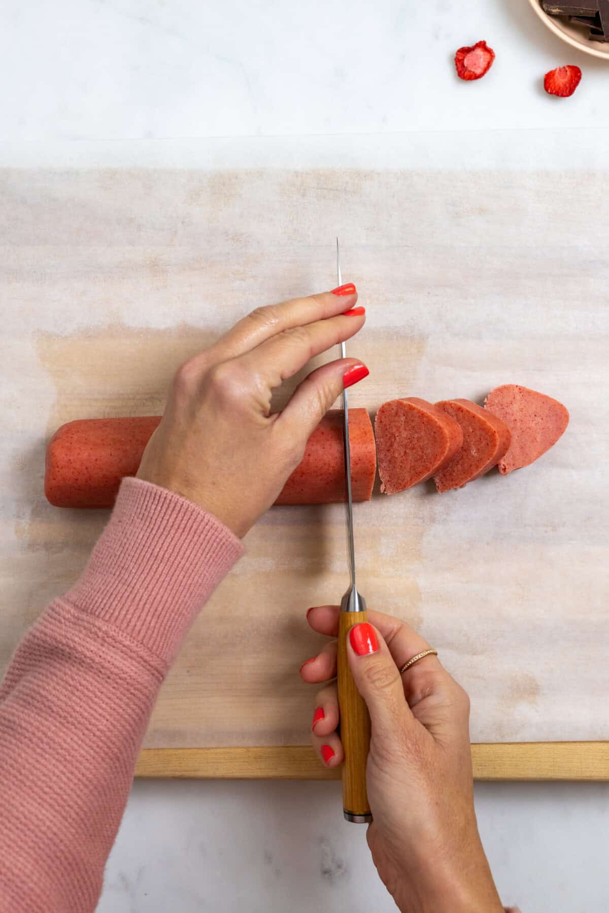 slicing strawberry shortbread cookie dough log into cookies