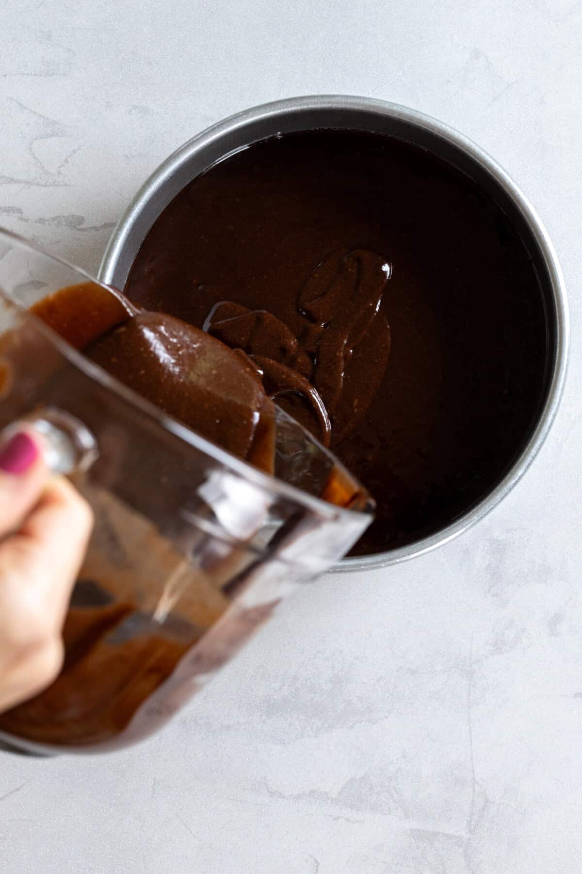 adding chocolate cake batter to a cake pan
